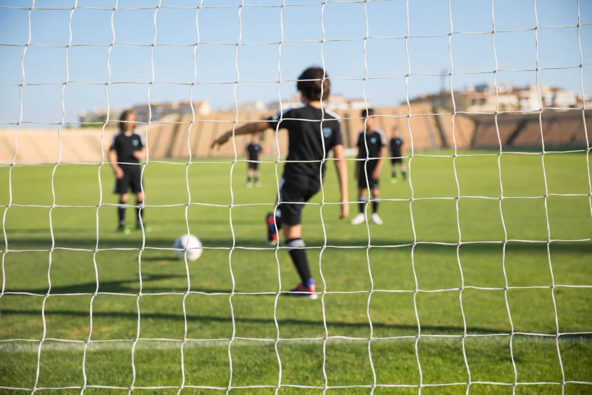Young players training on a sunny field, seen through the goal net